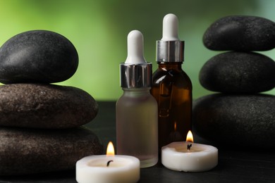 Photo of Spa composition with stones, droppers and burning candles on dark table against blurred green background, closeup