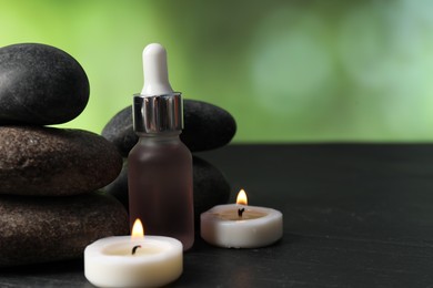 Photo of Spa composition with stones, dropper and burning candles on dark table against blurred green background, closeup. Space for text