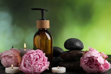 Photo of Spa composition with wet stones, burning candles and cosmetic product on dark table against blurred green background, closeup