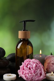 Photo of Spa composition with burning candles, flower and cosmetic product on table against blurred green background, closeup
