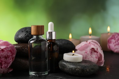 Photo of Spa composition with wet stones, cosmetic products and burning candles on dark table against blurred green background, closeup