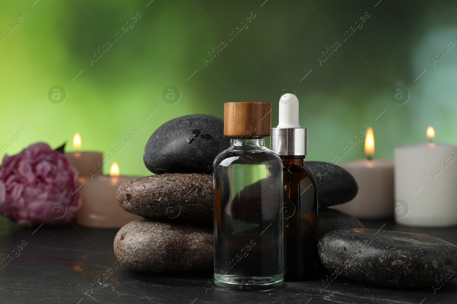 Spa composition with wet stones, cosmetic products and burning candles on dark table against blurred green background, selective focus Photo of Spa composition with wet stones, cosmetic products and burning candles on dark table against blurred green background, selective focus
