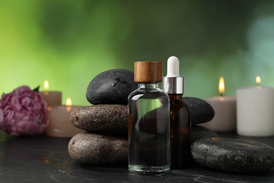 Photo of Spa composition with wet stones, cosmetic products and burning candles on dark table against blurred green background, selective focus