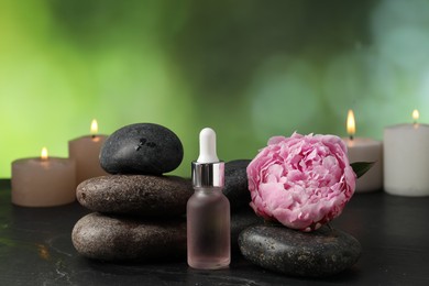 Photo of Spa composition with stones, dropper and flower on dark textured table against blurred green background, closeup