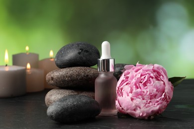 Photo of Spa composition with stones, dropper and flower on dark textured table against blurred green background, closeup