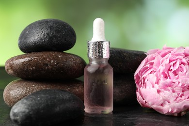 Photo of Spa composition with wet stones, dropper and flower on dark table against blurred green background, closeup