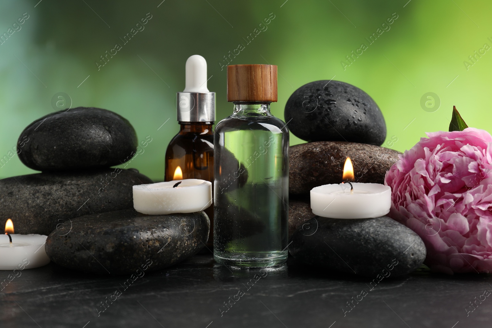 Spa composition with wet stones, cosmetic products and burning candles on dark textured table against blurred green background, closeup Photo of Spa composition with wet stones, cosmetic products and burning candles on dark textured table against blurred green background, closeup