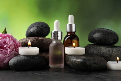 Photo of Spa composition with wet stones, cosmetic products and burning candles on dark textured table against blurred green background, closeup