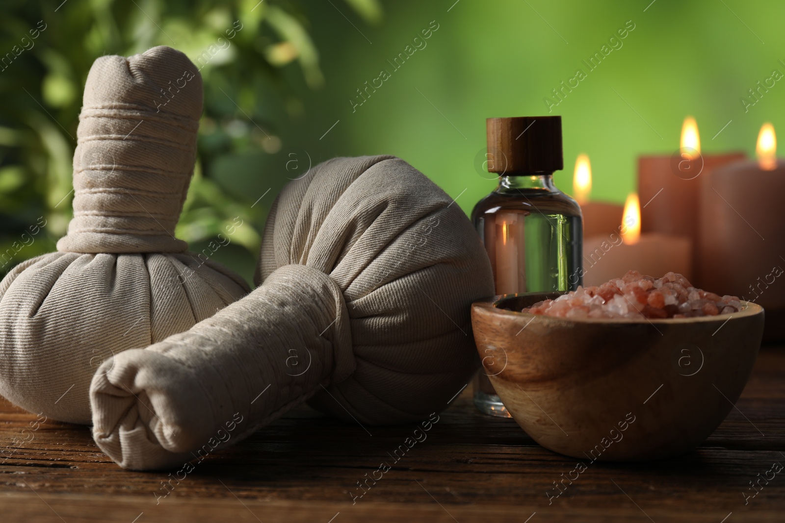 Photo of Spa composition with herbal bags and cosmetic products on wooden table against blurred green background, closeup