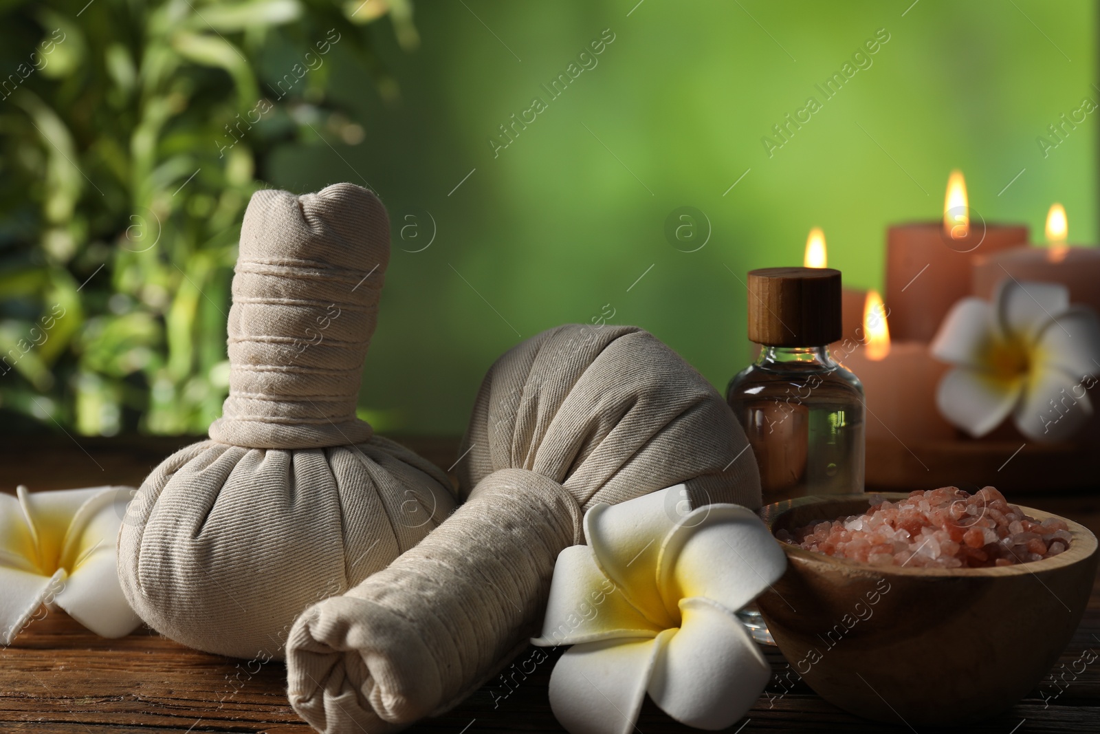 Photo of Spa composition with herbal bags and cosmetic products on wooden table against blurred green background, closeup