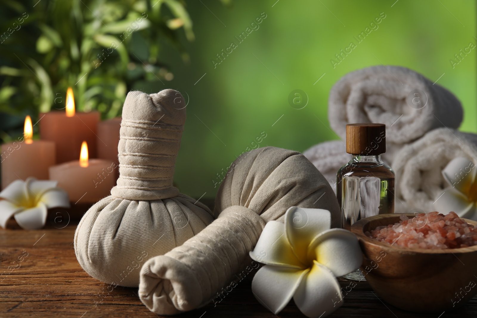 Spa composition with herbal bags and cosmetic products on wooden table against blurred green background, closeup Photo of Spa composition with herbal bags and cosmetic products on wooden table against blurred green background, closeup
