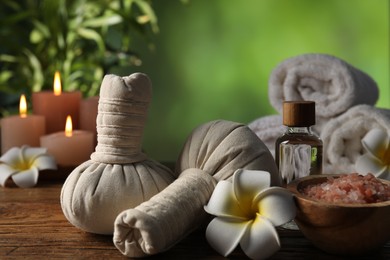 Photo of Spa composition with herbal bags and cosmetic products on wooden table against blurred green background, closeup