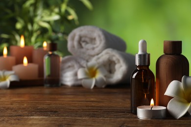 Photo of Spa composition with cosmetic products, flowers and burning candles on wooden table against blurred green background, selective focus