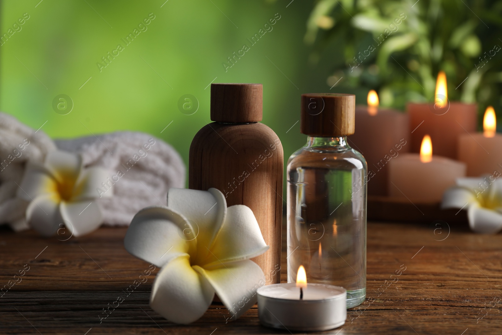 Photo of Spa composition with cosmetic products, flowers and burning candles on wooden table against blurred green background, closeup