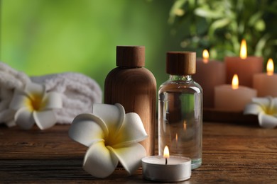 Photo of Spa composition with cosmetic products, flowers and burning candles on wooden table against blurred green background, closeup