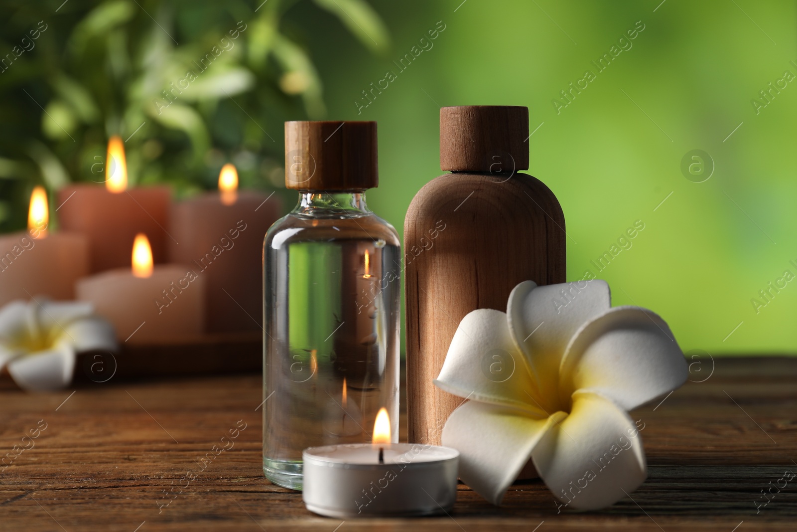 Spa composition with cosmetic products, flowers and burning candles on wooden table against blurred green background, closeup Photo of Spa composition with cosmetic products, flowers and burning candles on wooden table against blurred green background, closeup