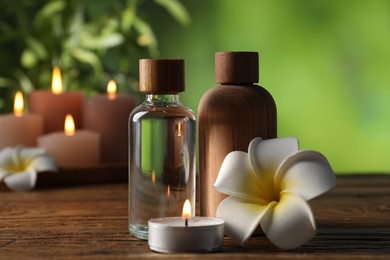 Photo of Spa composition with cosmetic products, flowers and burning candles on wooden table against blurred green background, closeup