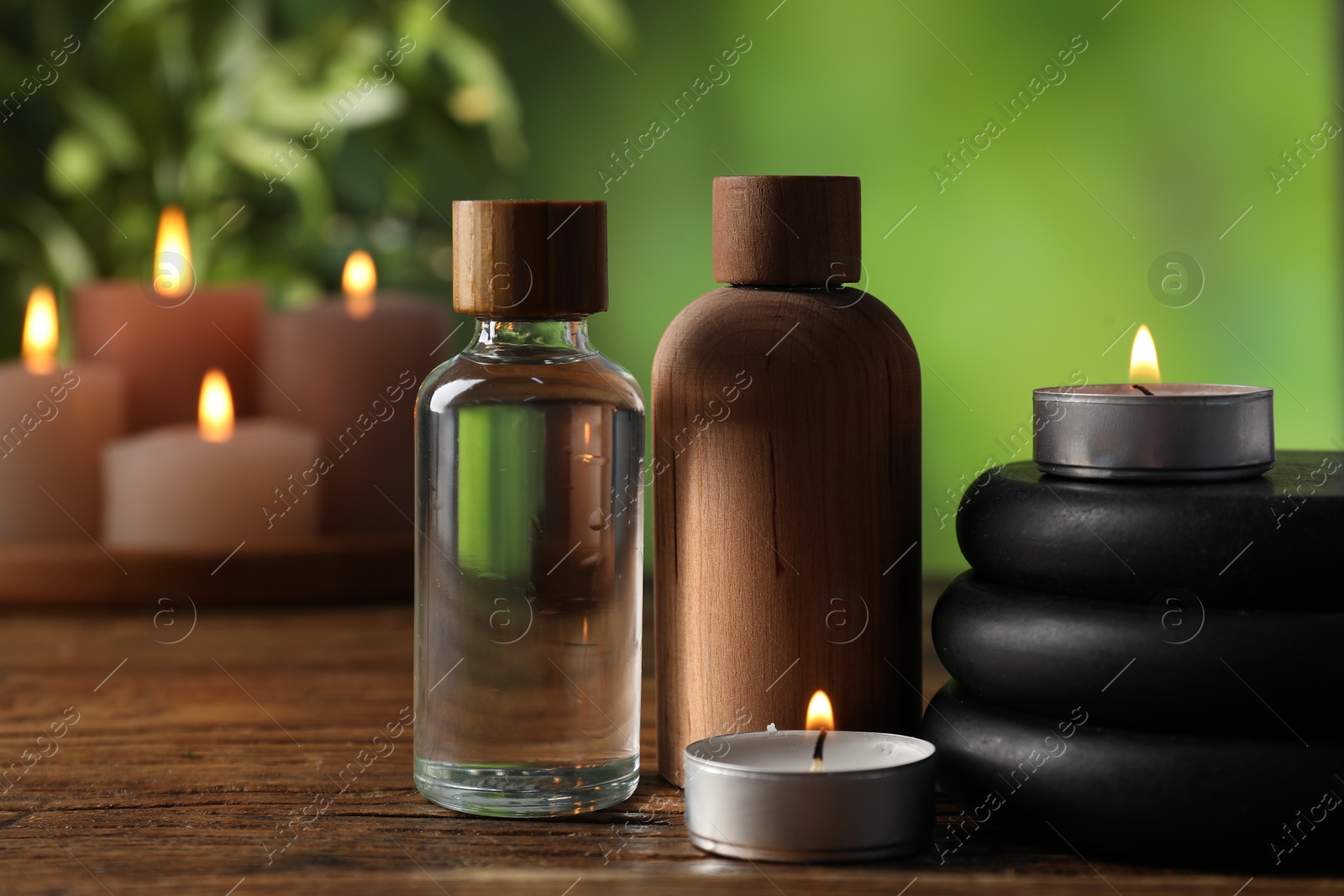 Spa composition with cosmetic products, stones and burning candles on wooden table against blurred green background, closeup Photo of Spa composition with cosmetic products, stones and burning candles on wooden table against blurred green background, closeup