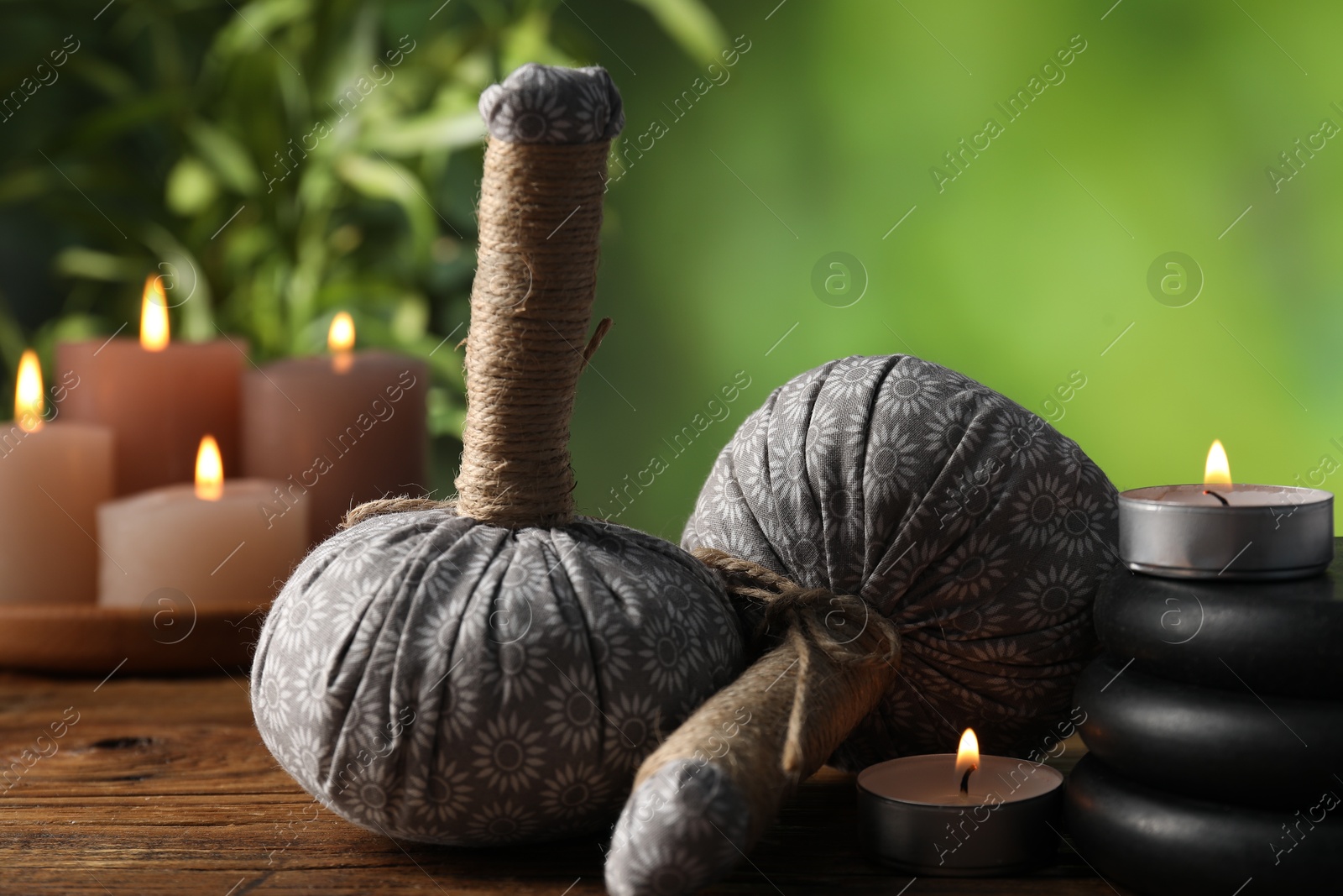 Spa composition with herbal bags, stones and burning candles on wooden table against blurred green background, closeup Photo of Spa composition with herbal bags, stones and burning candles on wooden table against blurred green background, closeup
