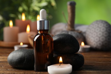Photo of Spa composition with dropper, stones and burning candle on wooden table against blurred green background, closeup