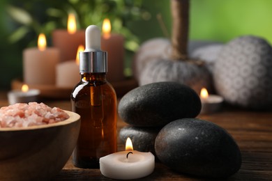 Photo of Spa composition with cosmetic products, stones and burning candle on wooden table against blurred green background, closeup