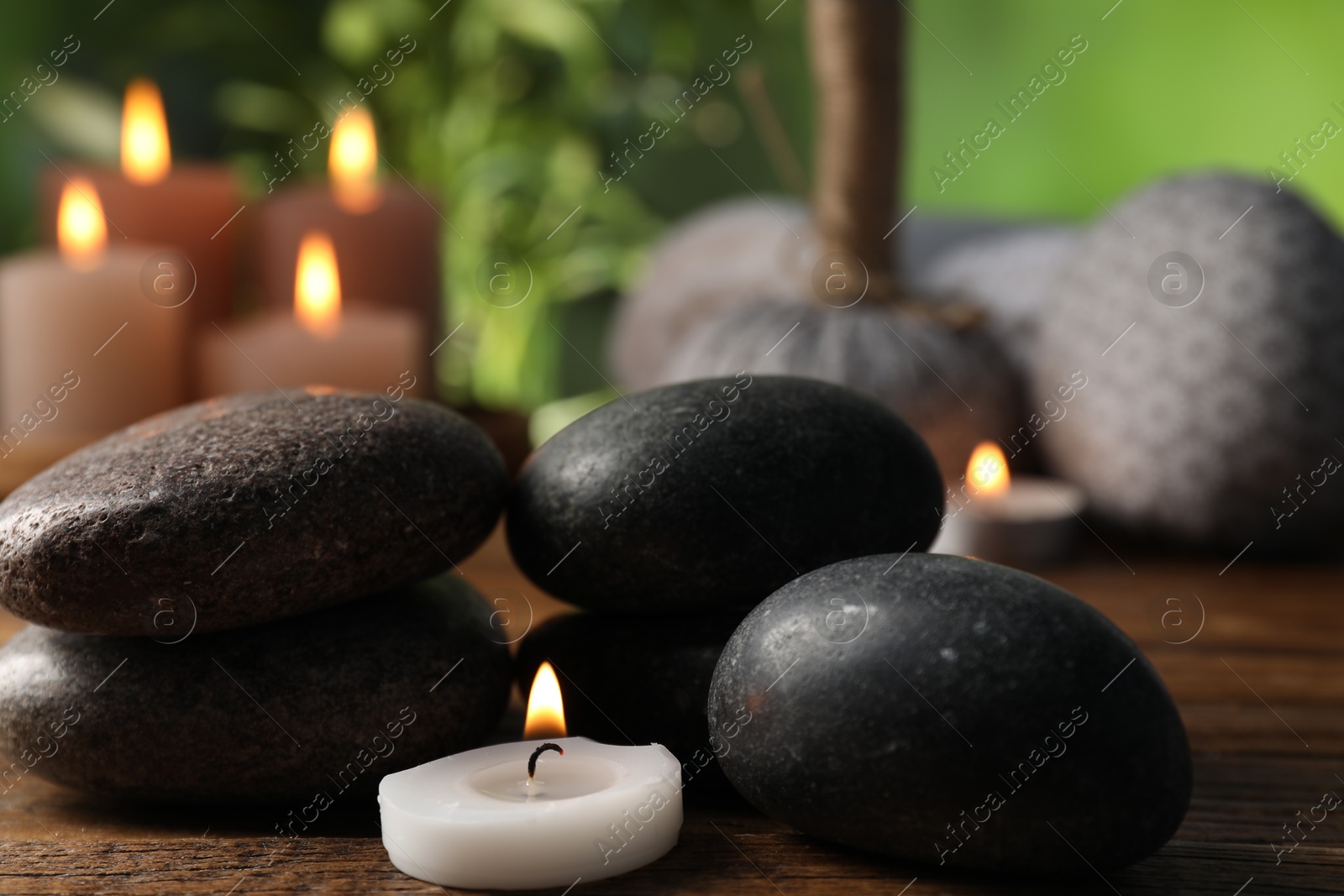 Spa composition with stones and burning candle on wooden table against blurred green background, closeup Photo of Spa composition with stones and burning candle on wooden table against blurred green background, closeup