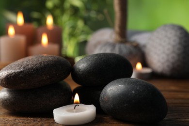 Photo of Spa composition with stones and burning candle on wooden table against blurred green background, closeup