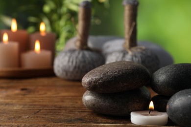 Photo of Spa composition with stones and burning candle on wooden table against blurred green background, closeup