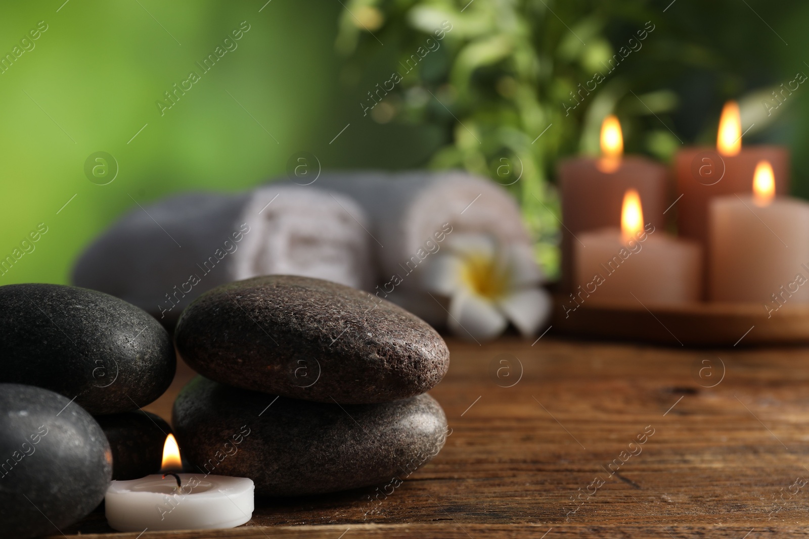 Spa composition with stones and burning candle on wooden table against blurred green background, closeup Photo of Spa composition with stones and burning candle on wooden table against blurred green background, closeup