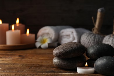 Photo of Spa composition with stones and burning candle on wooden table against black background, closeup