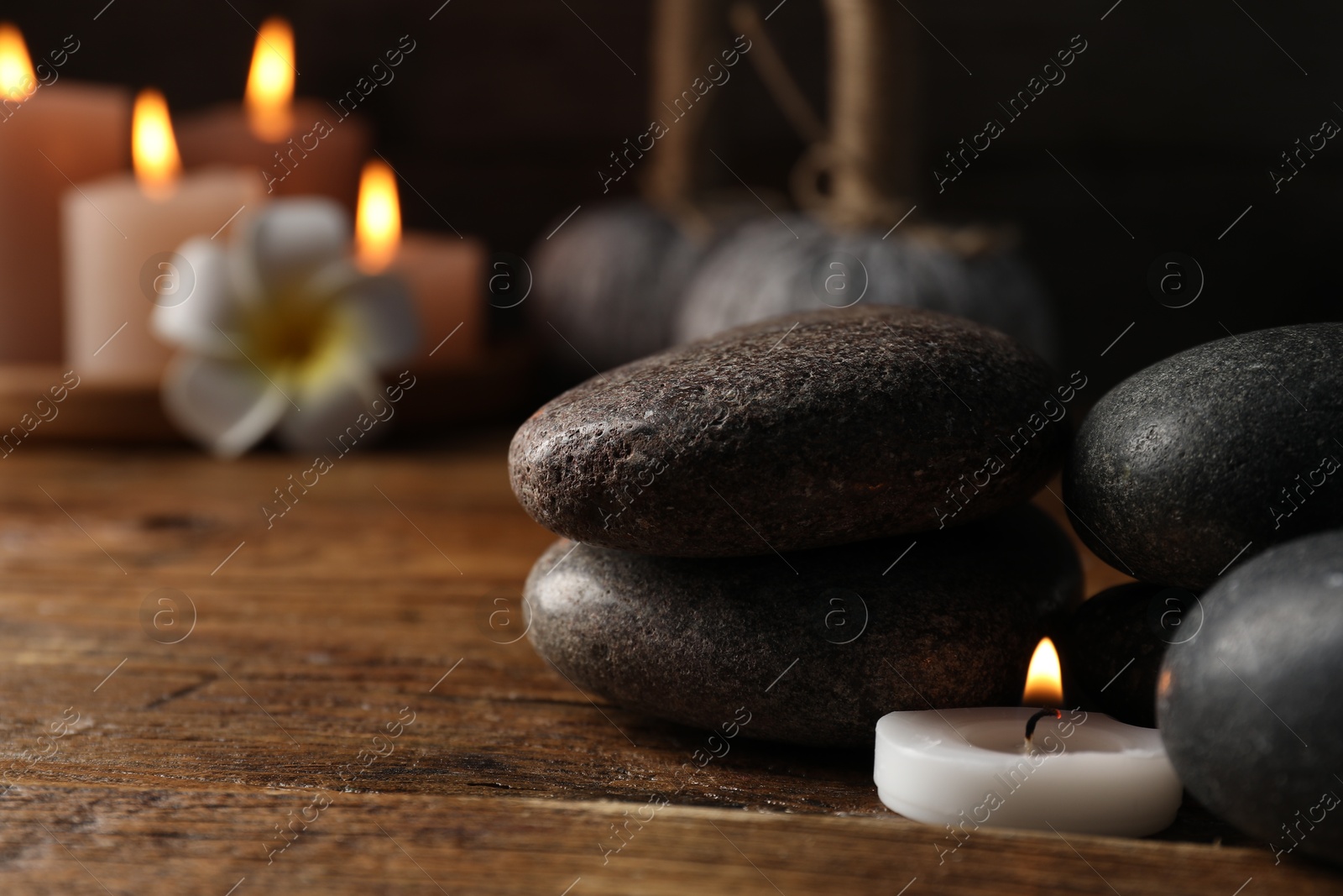 Spa composition with stones and burning candle on wooden table against black background, closeup Photo of Spa composition with stones and burning candle on wooden table against black background, closeup