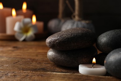 Photo of Spa composition with stones and burning candle on wooden table against black background, closeup