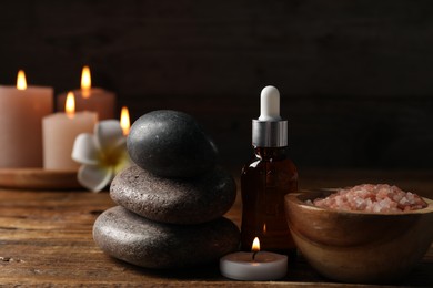 Photo of Spa composition with cosmetic products, stones and burning candle on wooden table against black background, closeup