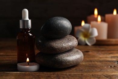 Photo of Spa composition with dropper, stones and burning candle on wooden table against black background, closeup