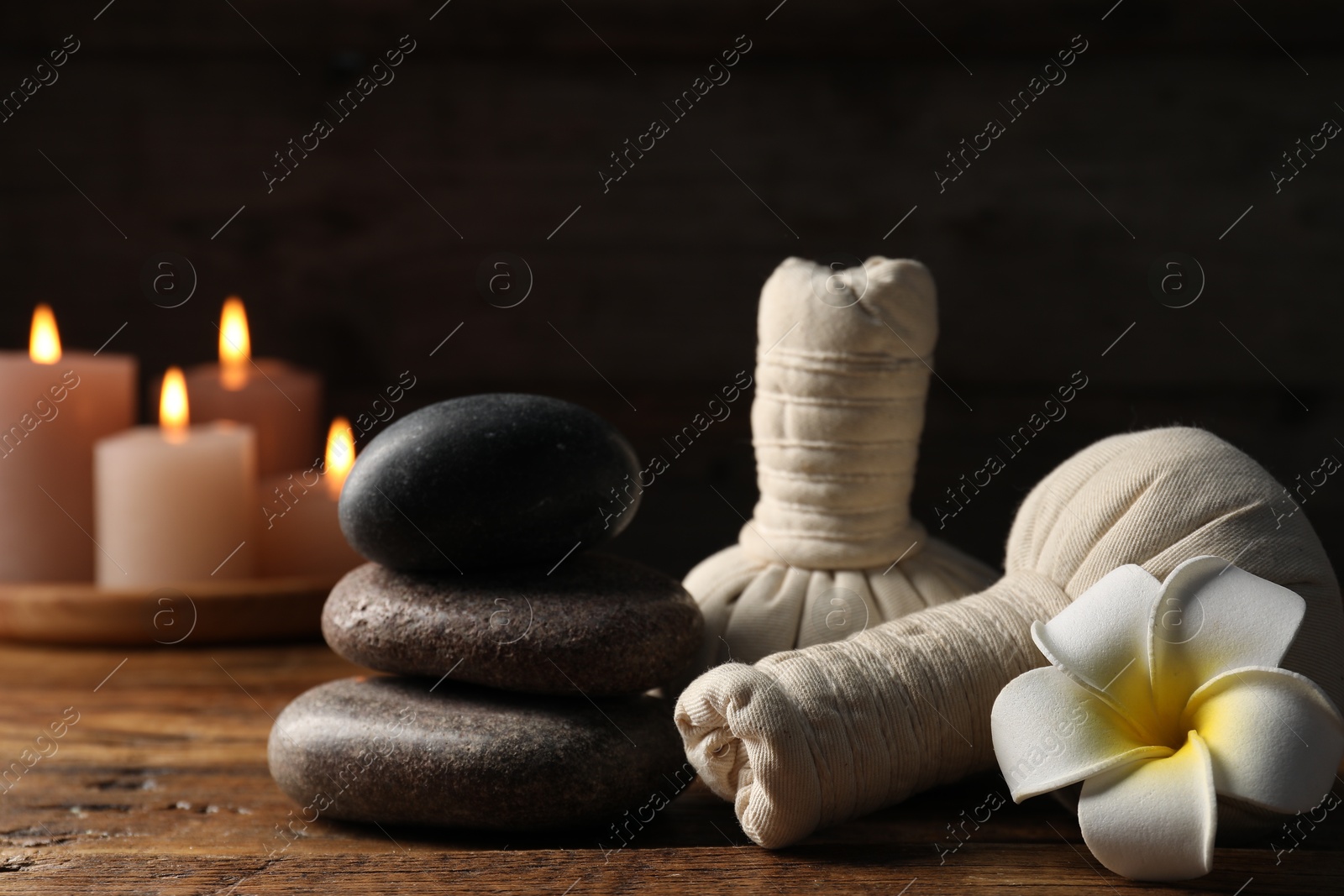 Spa composition with stones, flower and herbal bags on wooden table against black background, closeup Photo of Spa composition with stones, flower and herbal bags on wooden table against black background, closeup
