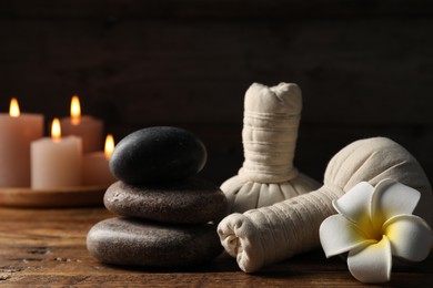 Photo of Spa composition with stones, flower and herbal bags on wooden table against black background, closeup