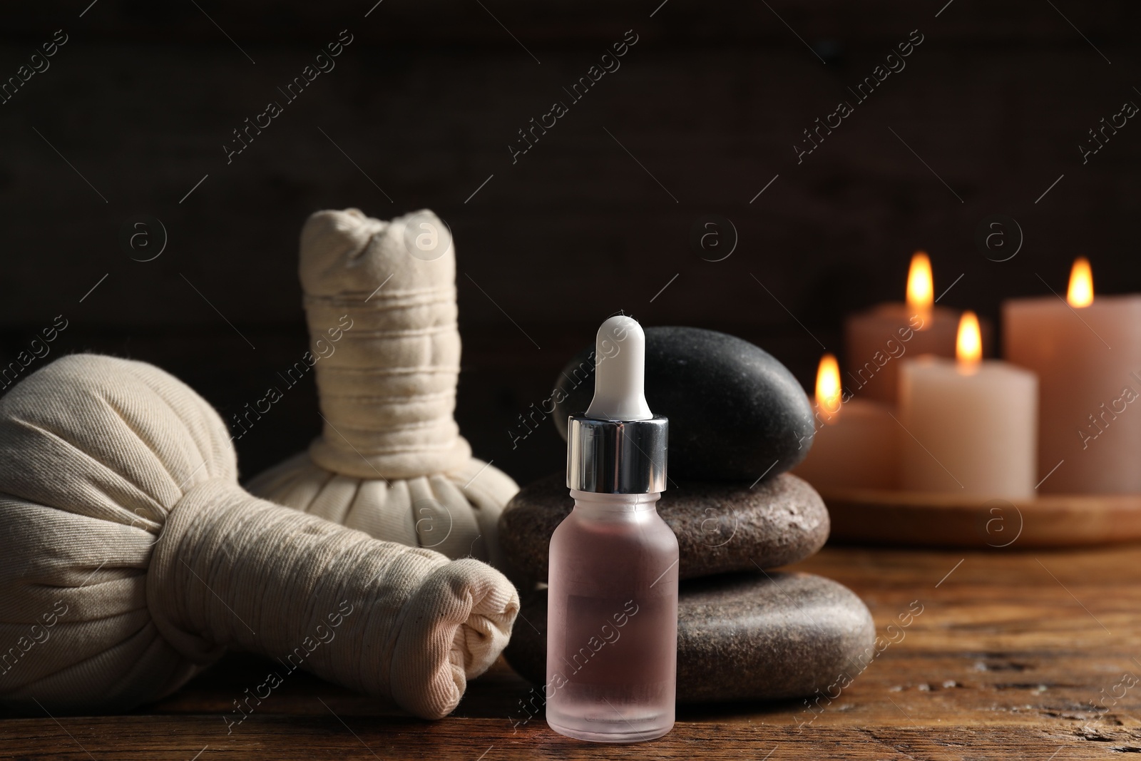 Spa composition with dropper, stones and herbal bags on wooden table against black background, closeup Photo of Spa composition with dropper, stones and herbal bags on wooden table against black background, closeup