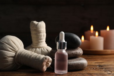 Photo of Spa composition with dropper, stones and herbal bags on wooden table against black background, closeup