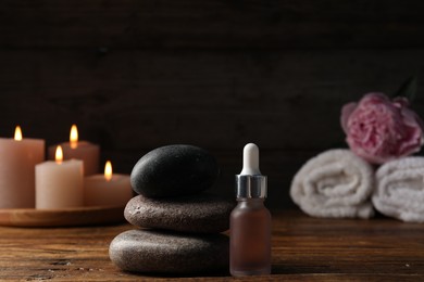Photo of Spa composition with stack of stones and dropper on wooden table against black background, closeup