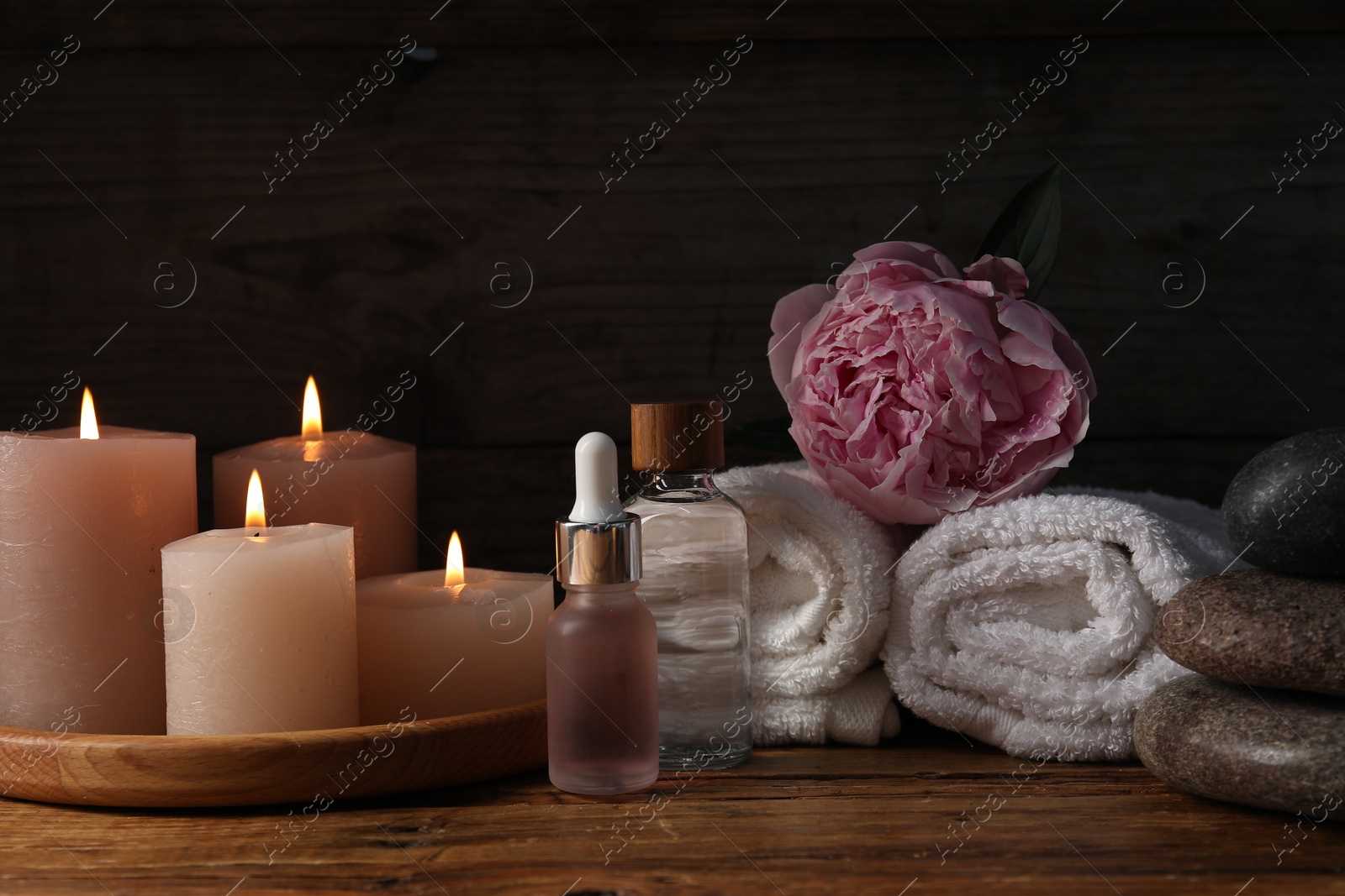 Spa composition with cosmetic products, burning candles and flower on wooden table against black background, closeup Photo of Spa composition with cosmetic products, burning candles and flower on wooden table against black background, closeup