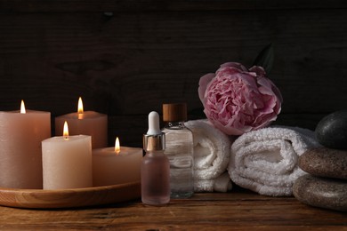 Photo of Spa composition with cosmetic products, burning candles and flower on wooden table against black background, closeup