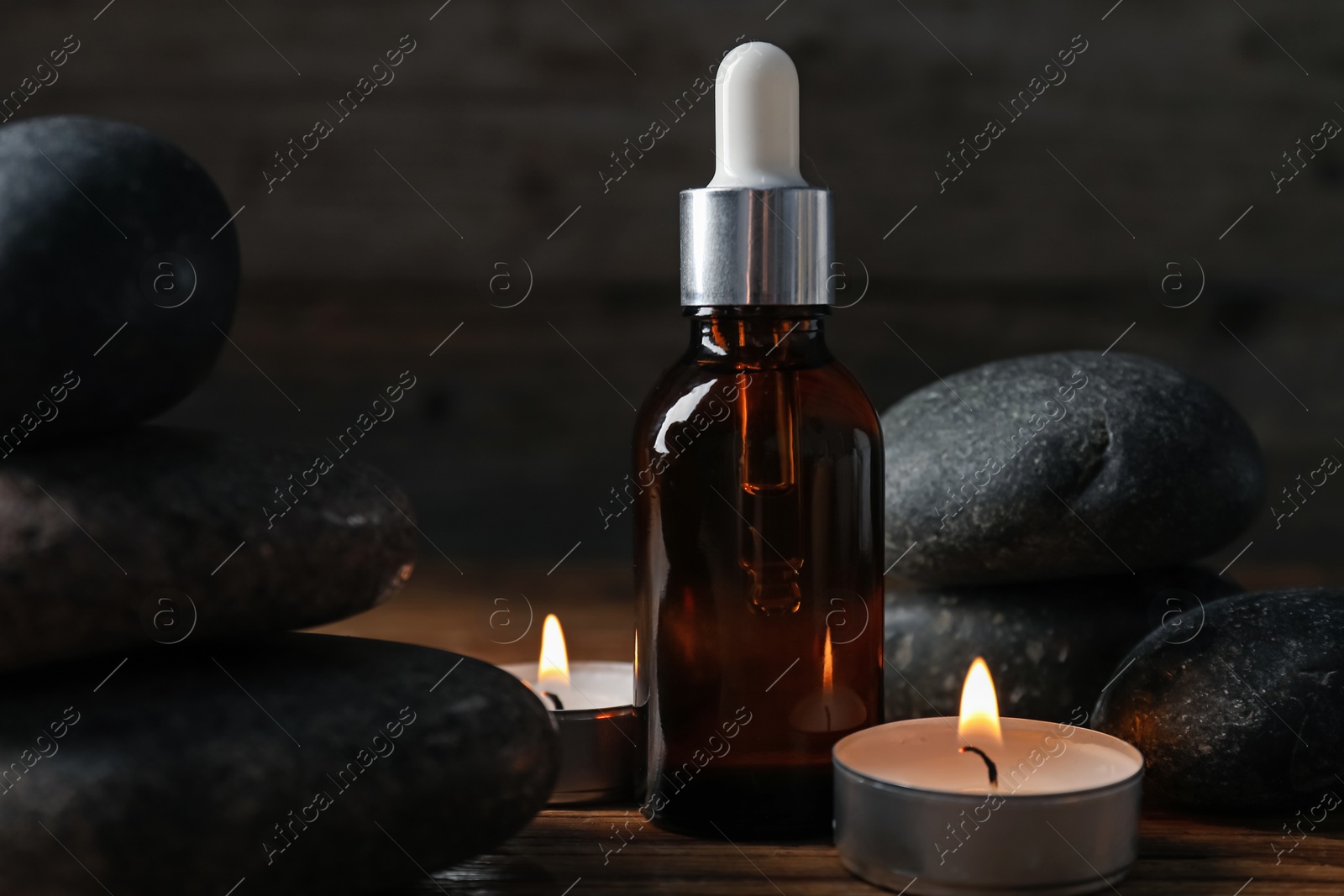 Spa composition with stones, dropper and burning candles on wooden table against black background, closeup Photo of Spa composition with stones, dropper and burning candles on wooden table against black background, closeup