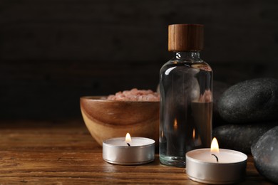 Photo of Spa composition with cosmetic products and burning candles on wooden table against black background, closeup