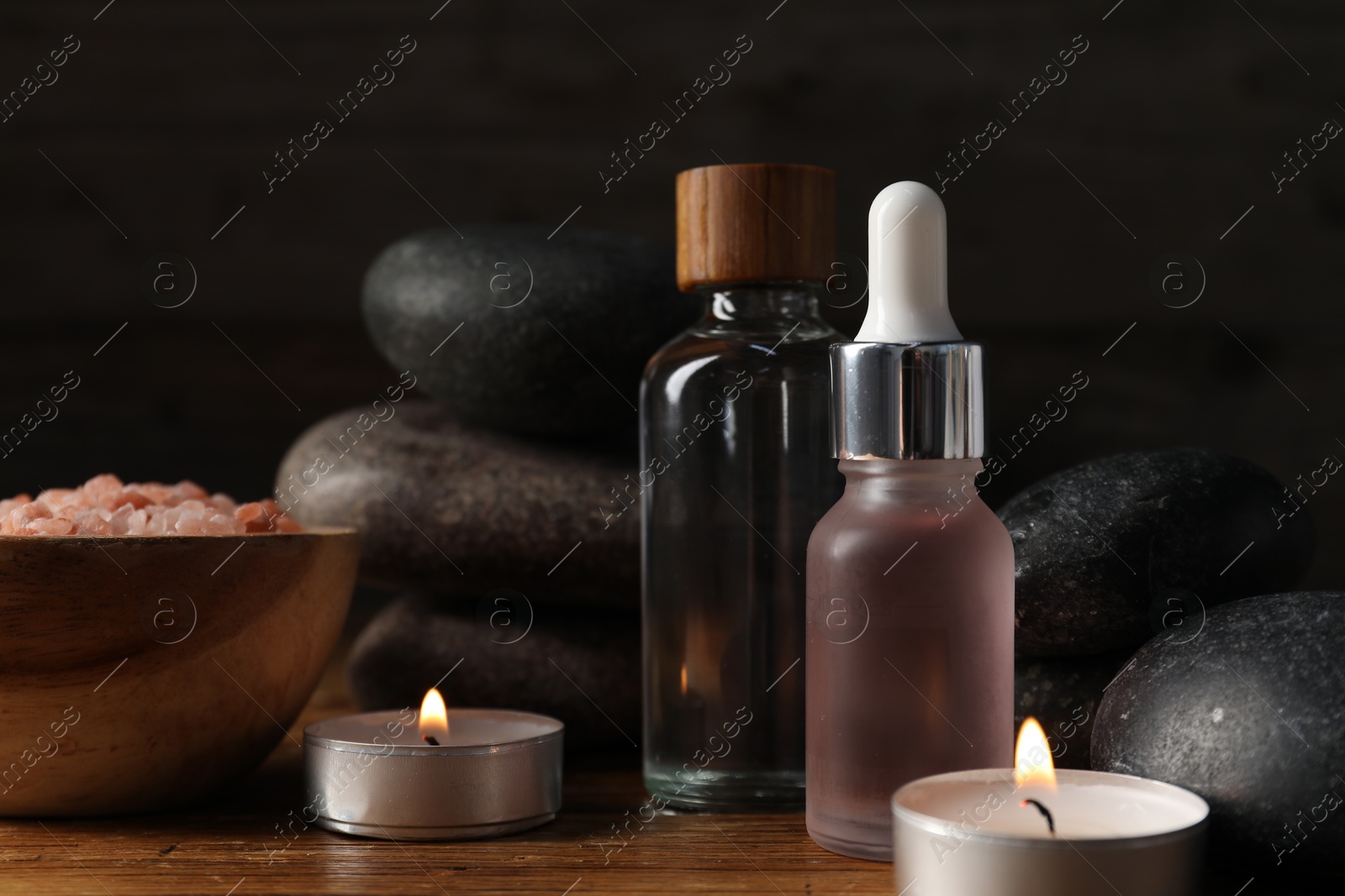 Spa composition with cosmetic products and burning candles on wooden table against black background, closeup Photo of Spa composition with cosmetic products and burning candles on wooden table against black background, closeup