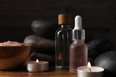 Photo of Spa composition with cosmetic products and burning candles on wooden table against black background, closeup