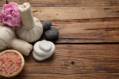 Photo of Spa composition with herbal bags, sea salt and stones on wooden table, above view. Space for text