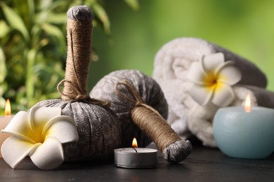 Photo of Spa composition with herbal bags, burning candles and plumeria flowers on grey textured table against blurred green background, closeup