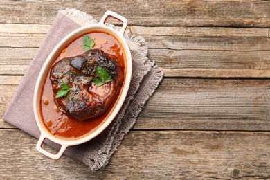Photo of Traditional ossobuco dish with beef steak and sauce on wooden table, top view. Space for text