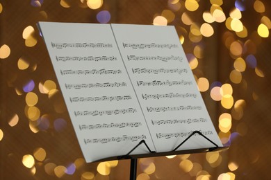 Photo of Note stand with music sheets against blurred lights, closeup. Bokeh effect