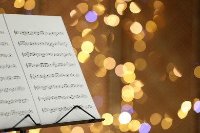 Photo of Note stand with music sheets against blurred lights, closeup. Space for text